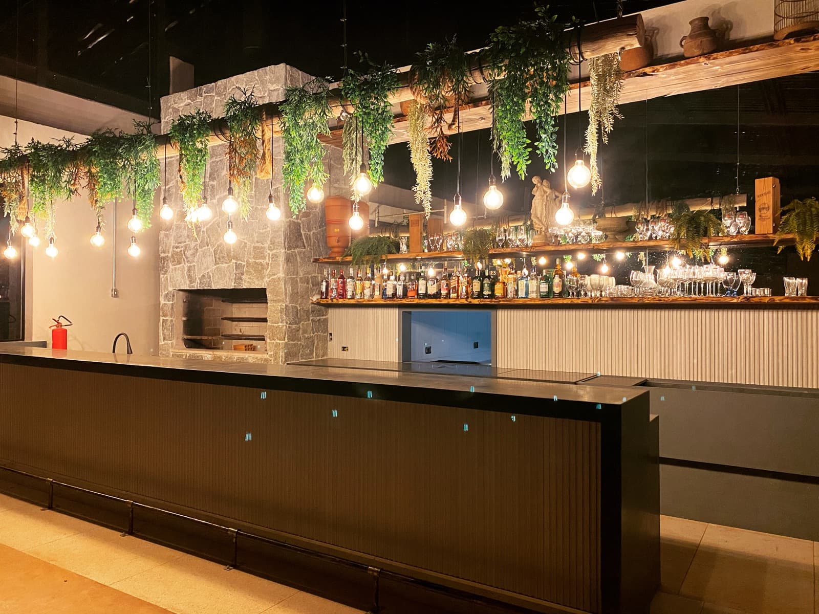 Bar de pedra da Xakara com chopeira, prateleiras iluminadas e plantas